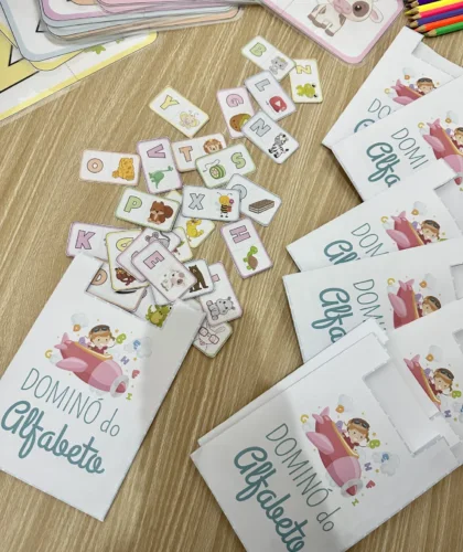 Peças do dominó do alfabeto espalhadas com cartas e lápis coloridos